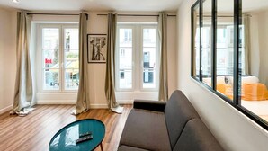 Ett modernt vardagsrum med en soffa, ett soffbord i glas och ett stort fönster med gardiner.
