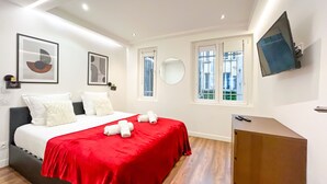 Ett modernt hotellrum med en säng, ett skrivbord, en TV och ett fönster med utsikt över byggnader.