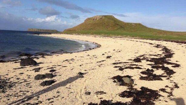 Una playa con arena, una colina pequeña y una masa de agua.