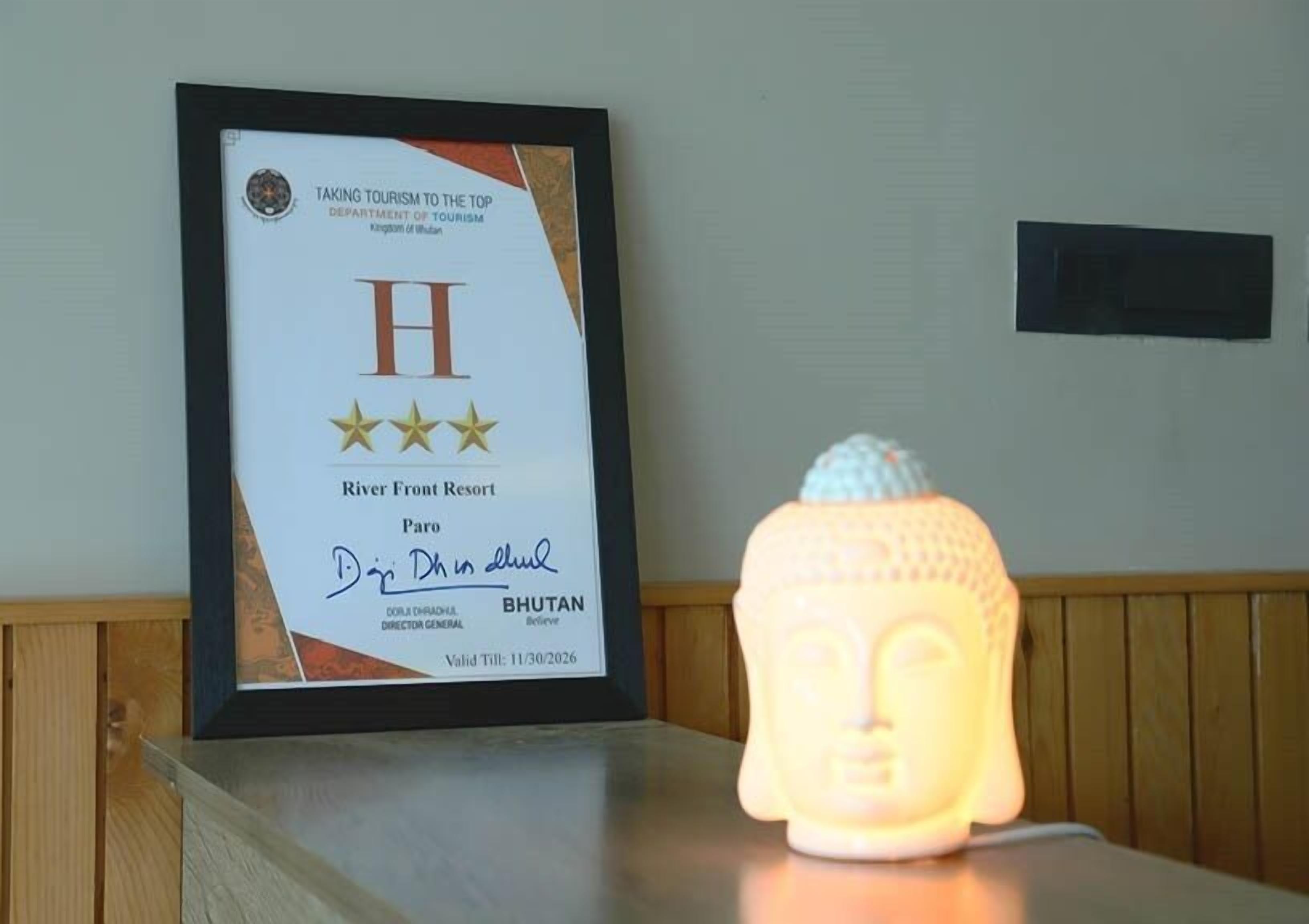 Een lijst met een certificaat aan een muur, een Boeddhabeeld en een houten paneel.