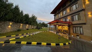 A hotel with a traditional architectural style, a well-maintained lawn, and a clear view of the mountains in the background. - River Front Resort (Paro)
