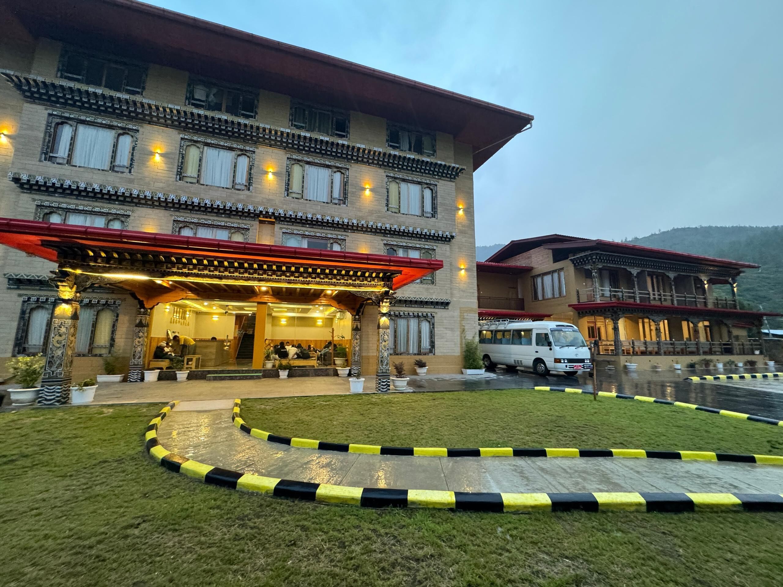 A multi-story hotel with a traditional architectural style, featuring a covered entrance and a parking area.