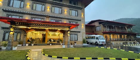 A multi-story hotel with a traditional architectural style, featuring a covered entrance and a parking area.