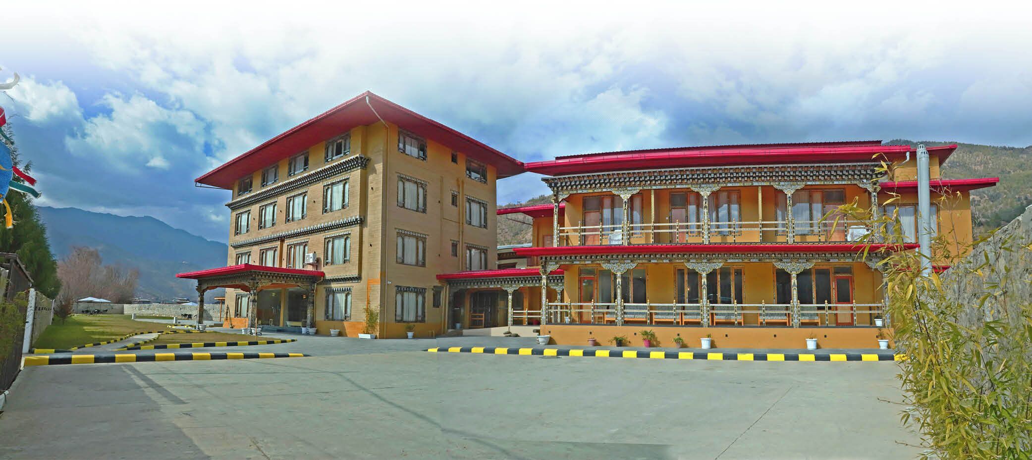 A multi-story building with a red roof, a balcony with ornate railings, and a parking area with yellow and black curbs.