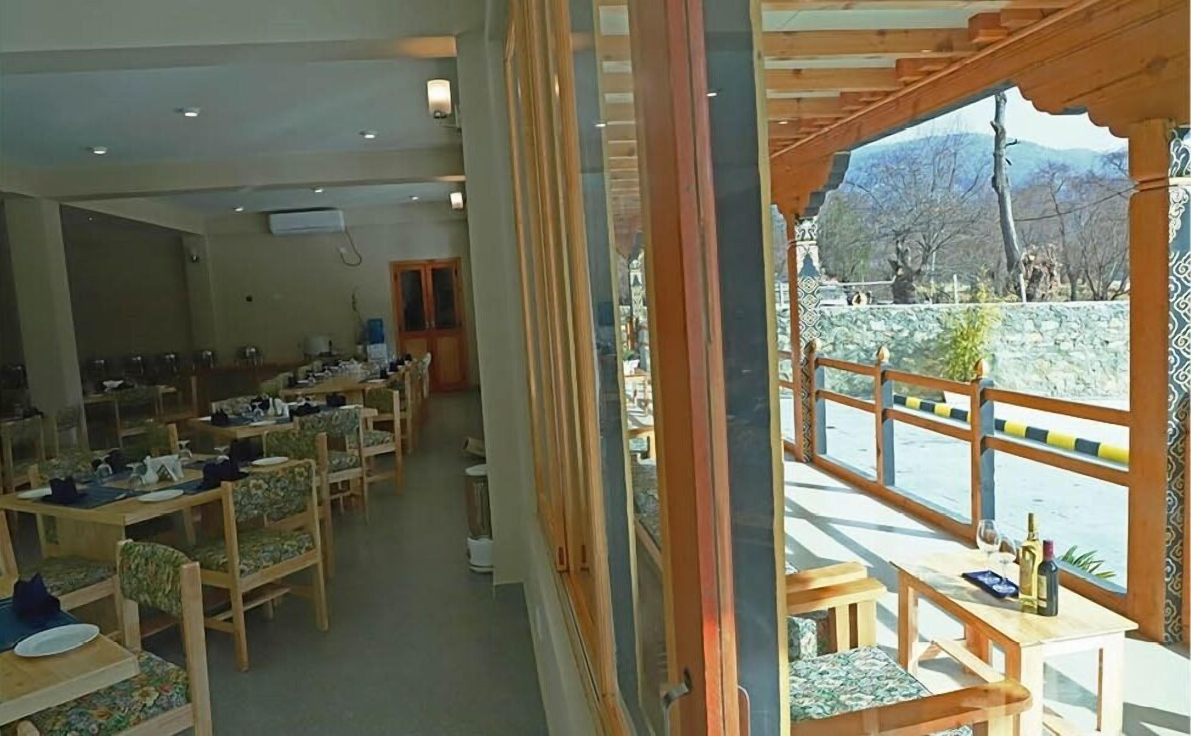 A dining area with multiple tables and chairs, a view of the outdoors through a window, and a door leading to another room.
