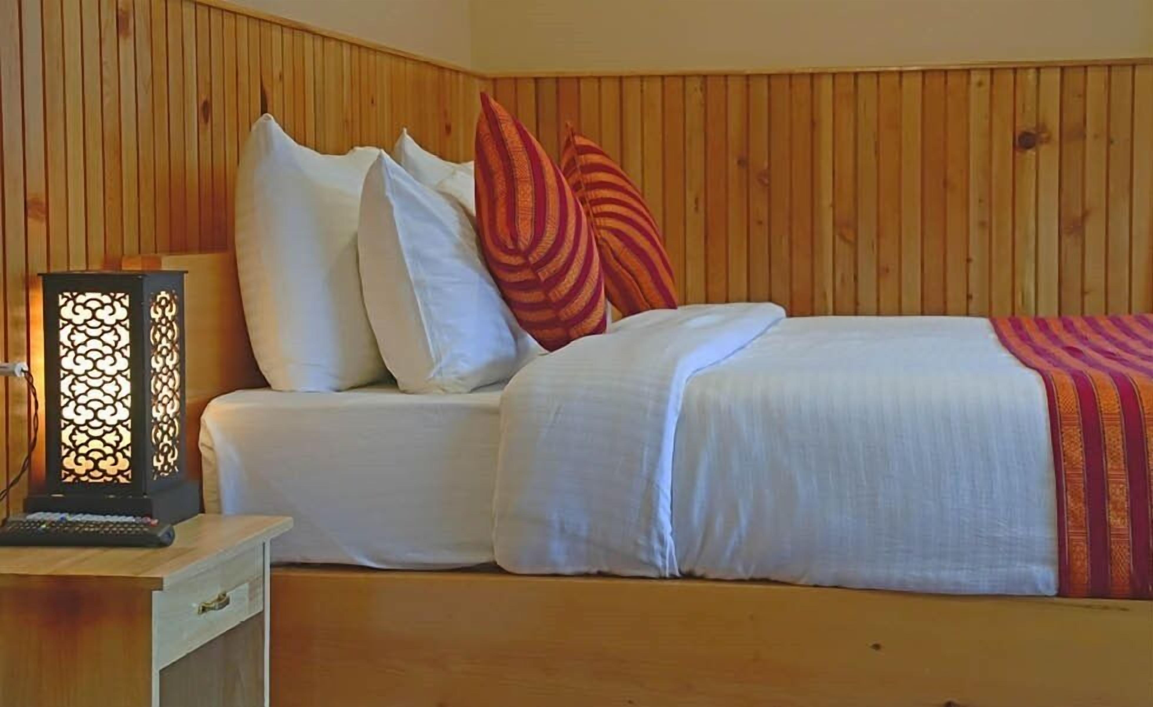 A wooden-paneled room with a bed, pillows, and a nightstand with a lamp.