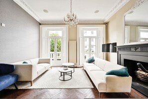 A living room with a fireplace, two sofas, a coffee table, and a chandelier. - 5 Beds House - 5 Mins to Victoria Station (London)