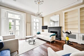 A spacious living room with a white sofa, a small round table, a fireplace, and a bike rack. - 5 Beds House - 5 Mins to Victoria Station (London)
