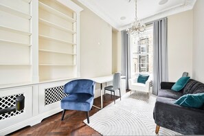 Ein modernes Wohnzimmer mit einem weißen Schreibtisch, einem blauen Sessel, einem grauen Sofa und einem gemusterten Teppich.