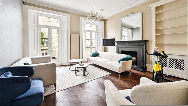 A living room with a white sofa, blue armchair, and a yellow bicycle. - 5 Beds House - 5 Mins to Victoria Station (London)