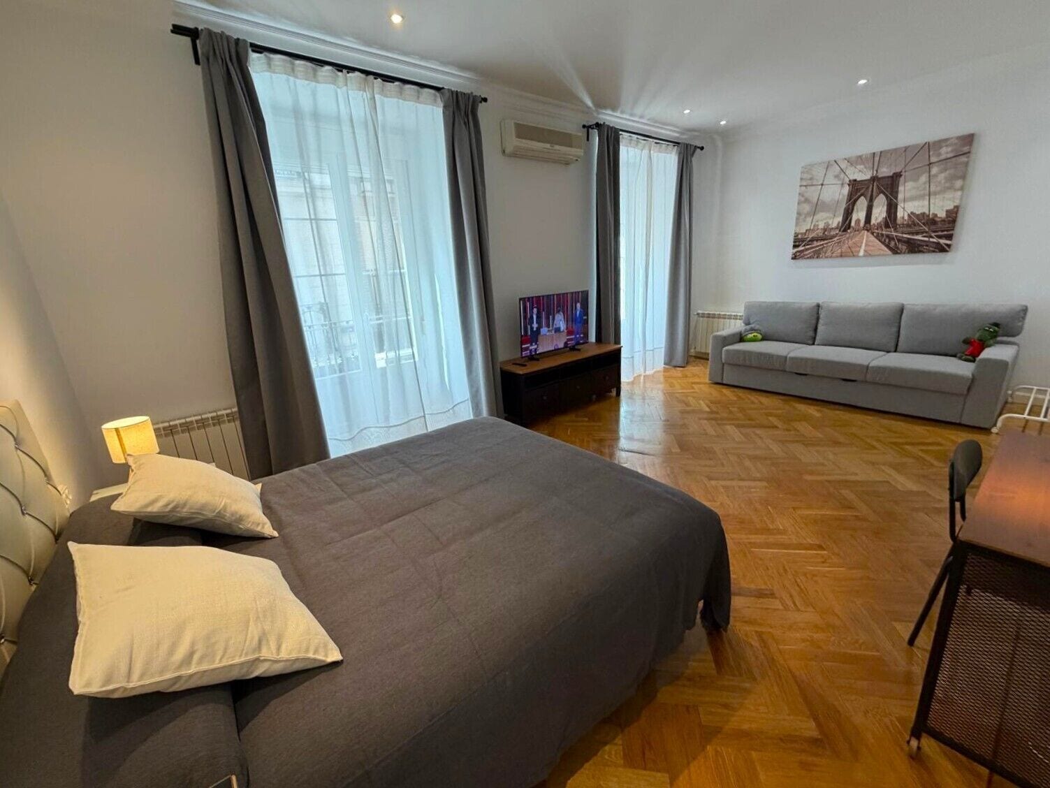 Ein Schlafzimmer mit Bett, Sofa, Fernseher und einem Bild an der Wand.