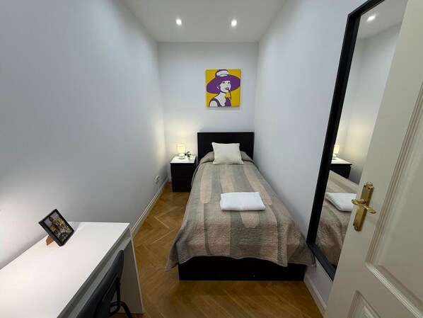 A bedroom with a bed, bedside tables, a desk, and a mirror. - Habitaciones Libertad (Madrid)