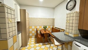 Una cocina compacta con una mesa, sillas, un reloj y una pequeña planta en maceta.