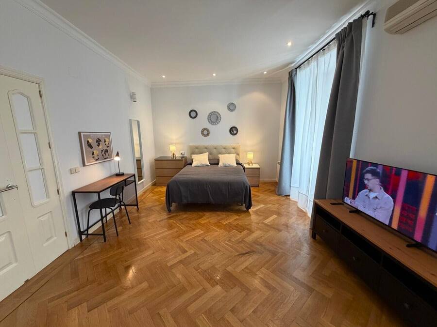 A bedroom with a bed, bedside tables, a desk, and a TV.