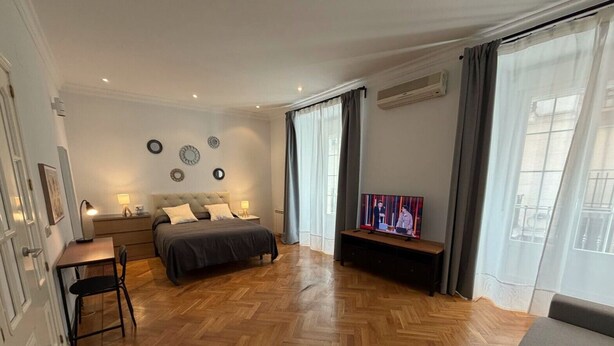 Un dormitorio con cama, mesitas de noche, escritorio, silla, televisor y sofá.