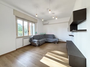 Una habitació àmplia amb un gran finestral, un sofà gris i un moble prestatge integrat.