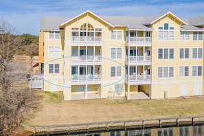 A multi-story building with balconies, a flat roof, and a grassy area in front.
