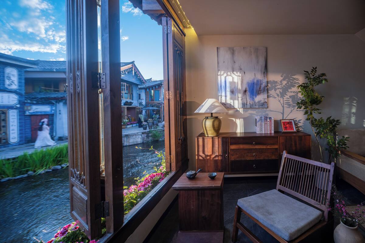 A room with a large window, a wooden cabinet, a chair, and a table.