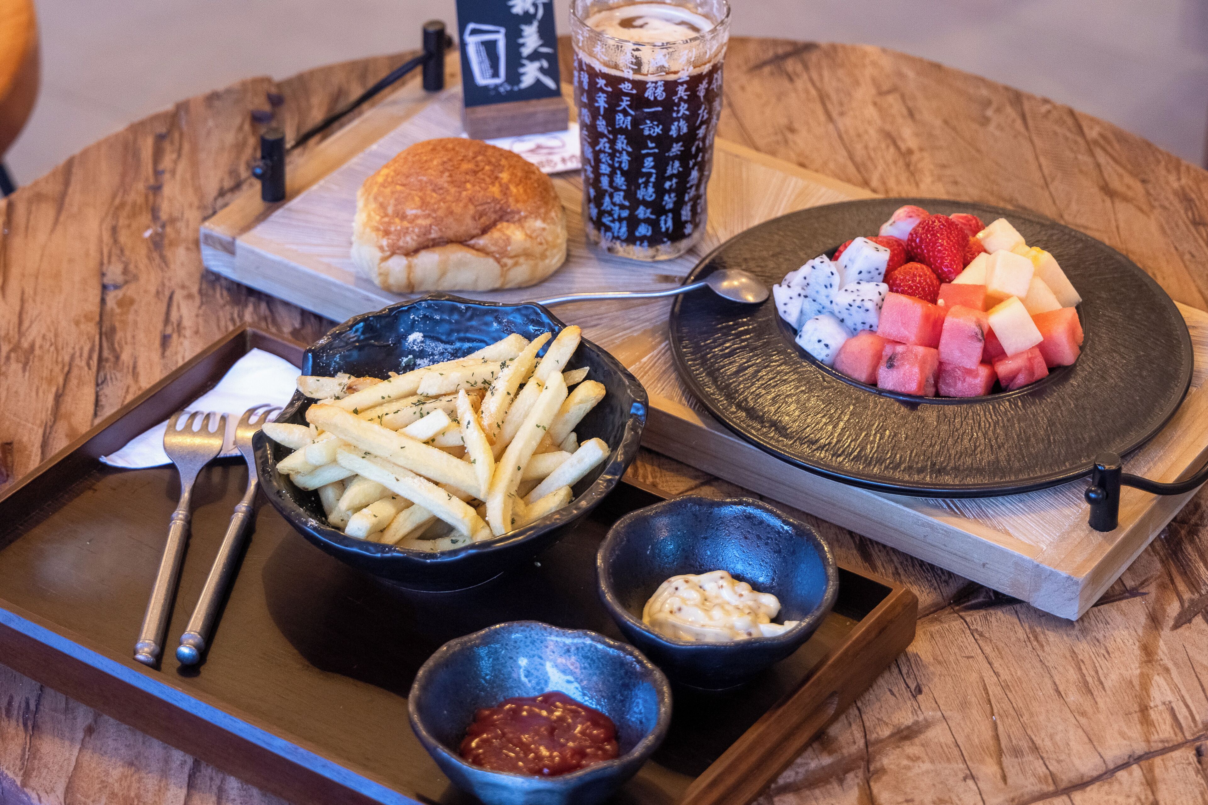 Een dienblad met eten, waaronder friet, een hamburger en een fruitschaal, samen met sauzen en een drankje.