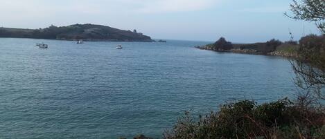 A coastal landscape with calm water, rocky outcrops, and distant hills.