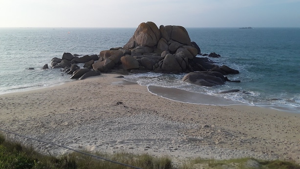 Een strand met grote rotsen, een zandstrand en een rustige zee.