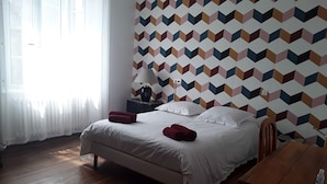 Een slaapkamer met een bed, nachtkastje, lamp en een behang met patroon.
