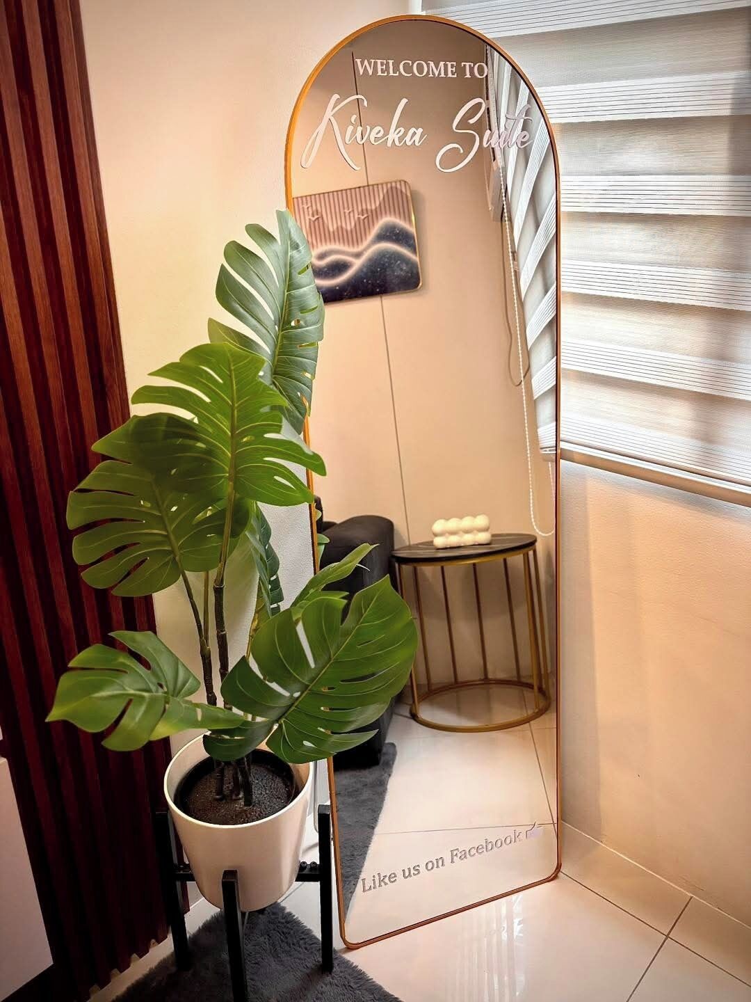 A potted plant, a mirror with a welcome sign, and a small table with a stool.