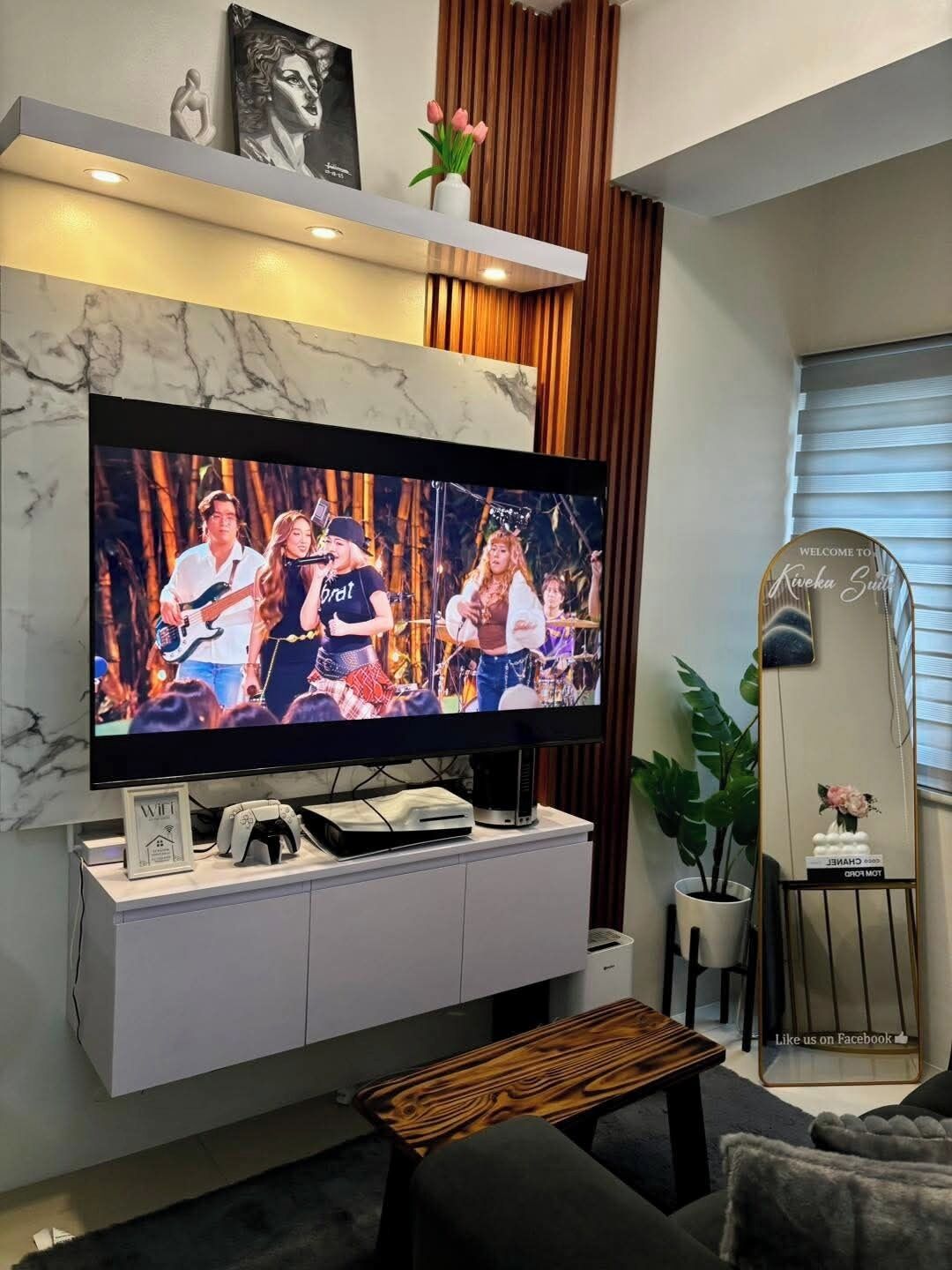 Una sala de estar moderna con un televisor de pantalla plana grande, un mueble blanco para el equipo multimedia, una mesa de centro de madera y una planta en maceta.