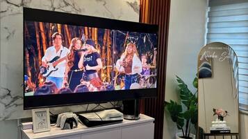 Una sala de estar moderna con un televisor de pantalla plana grande, un mueble blanco para el equipo multimedia, una mesa de centro de madera y una planta en maceta.