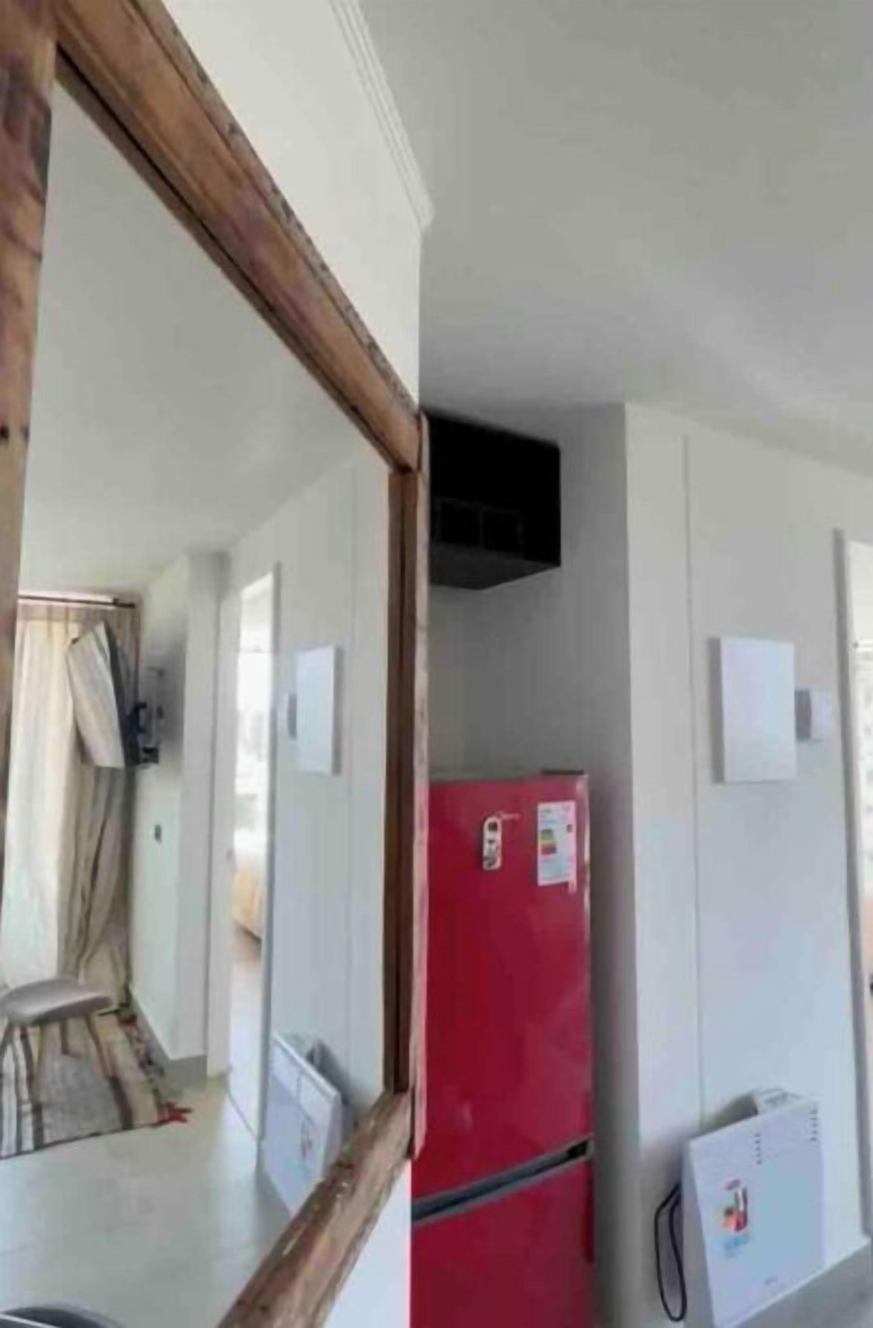 Une pièce avec un réfrigérateur rouge, un climatiseur blanc fixé au mur et un miroir encadré en bois.