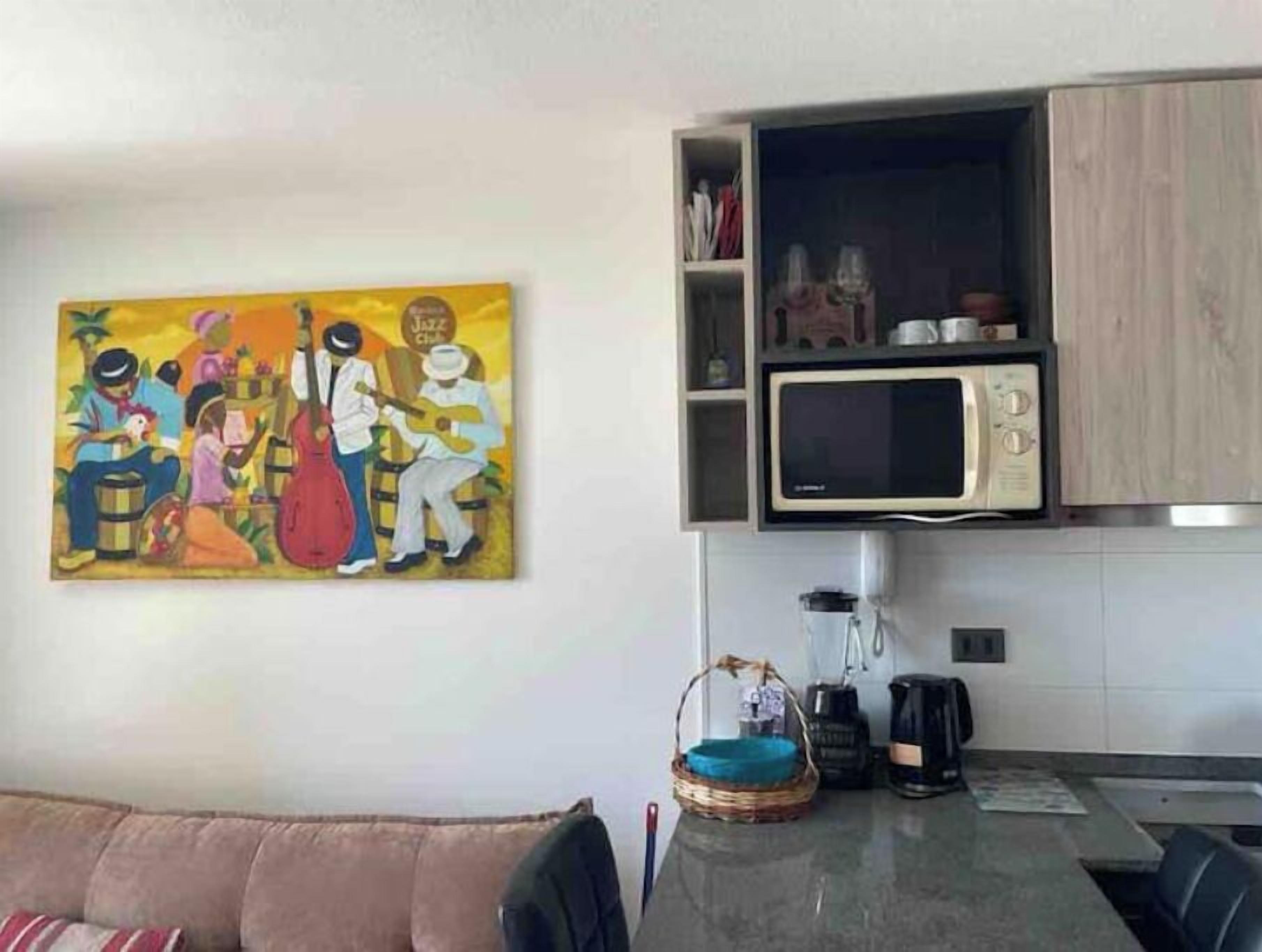 Ein Wohnzimmer mit Sofa, Couchtisch, einem Bild und einer Küchenzeile inklusive Mikrowelle und Schränken.