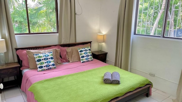 A bedroom with a bed, pillows, a nightstand, a lamp, and a window with curtains. - Close to shops and Restaurants, Family friendly, 5 minutes to beach (Holetown)
