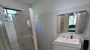 A modern bathroom with a glass-enclosed shower, a white sink with a mirror above, and a tiled floor. - Close to shops and Restaurants, Family friendly, 5 minutes to beach (Holetown)