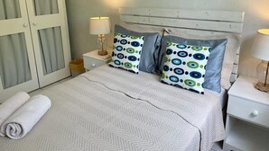 A bed with a chevron-patterned bedspread, two pillows with a circular pattern, a nightstand with a lamp, and a door with frosted glass panels. - Close to shops and Restaurants, Family friendly, 5 minutes to beach (Holetown)