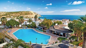 A resort with a large swimming pool, lounge chairs, palm trees, and a view of the sea. - 1D Waterside with Shared Pool (Luz)