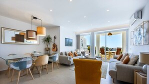 A modern living room with a glass dining table, sofas, and a yellow armchair. - 1D Waterside with Shared Pool (Luz)