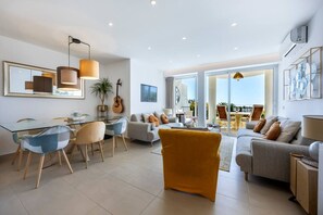 A modern living room with a glass dining table, sofas, and a yellow armchair. - 1D Waterside with Shared Pool (Luz)