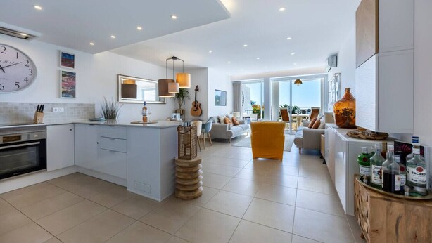 A modern kitchen with a central island, a dining area with a sofa, and a living room with a view. - 1D Waterside with Shared Pool (Luz)