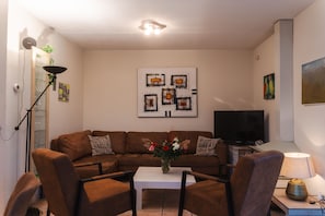 A living room with a brown sofa, a white coffee table, and a TV. - Villa KAREKIET in a prime location in Sint Maartenszee for 8 people (Sint Maartensvlotbrug)