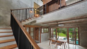 Un interior amplio con una escalera de madera, un comedor y ventanas grandes que ofrecen vistas al verdor.