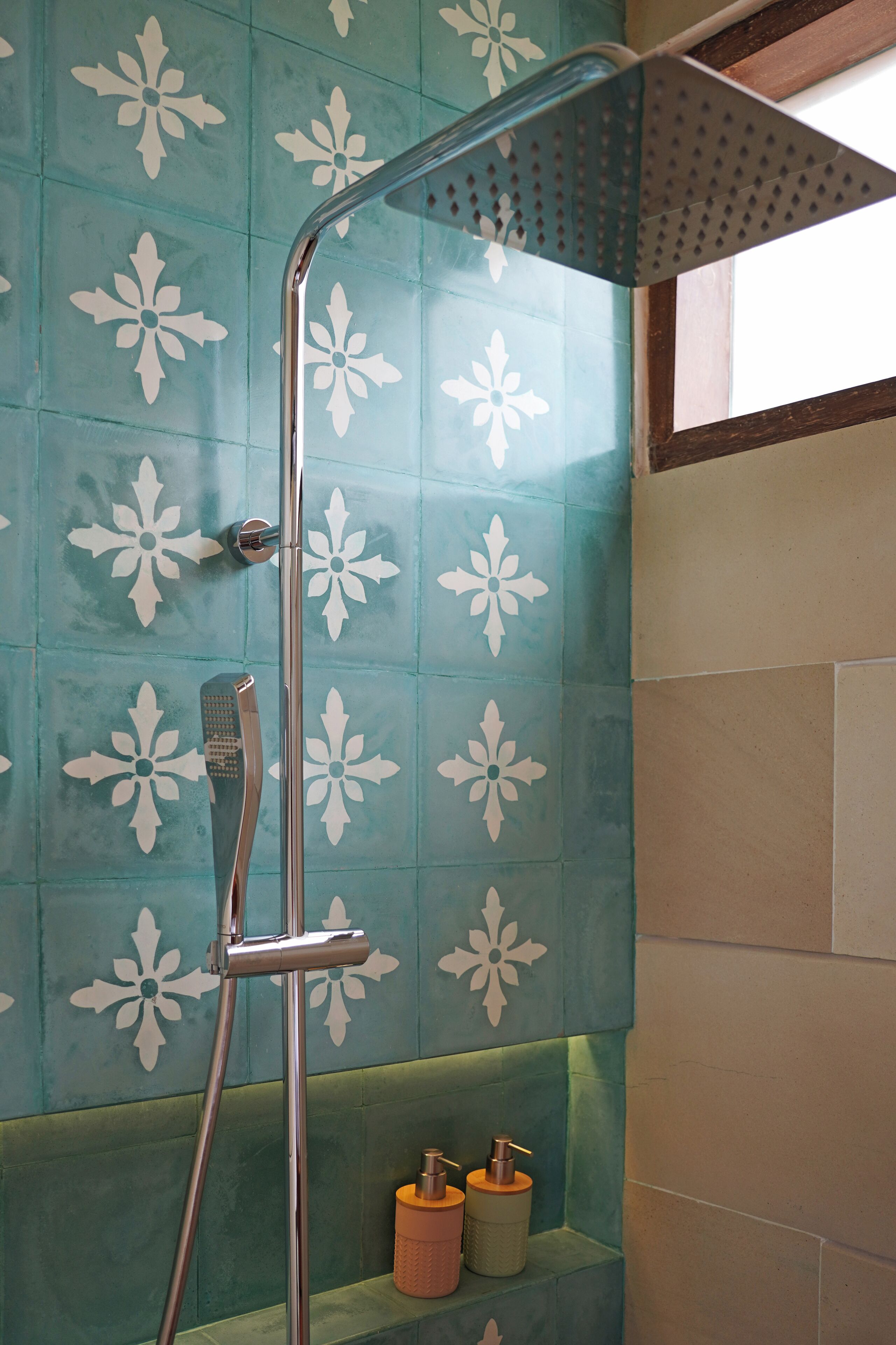 A shower with a chrome handle and a glass door, set against a wall with a floral tile pattern.
