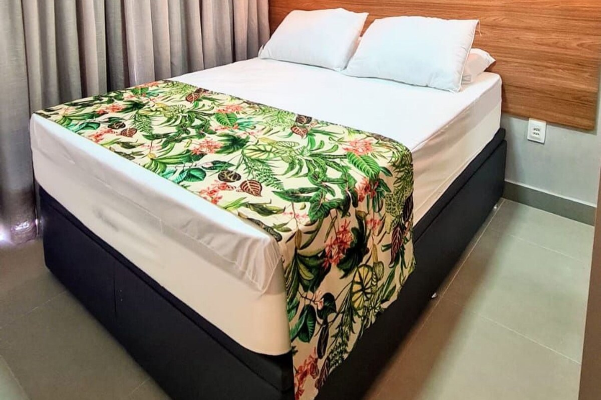 Une chambre d’hôtel moderne avec un grand lit, une tête de lit en bois, une couvre-lit à motifs floraux et un luminaire suspendu.