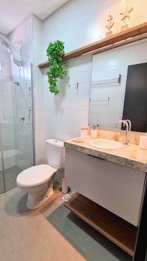 Ein modernes Badezimmer mit Duschkabine aus Glas, Toilette, Waschbecken mit Spiegel und einer kleinen Zimmerpflanze an der Wand.