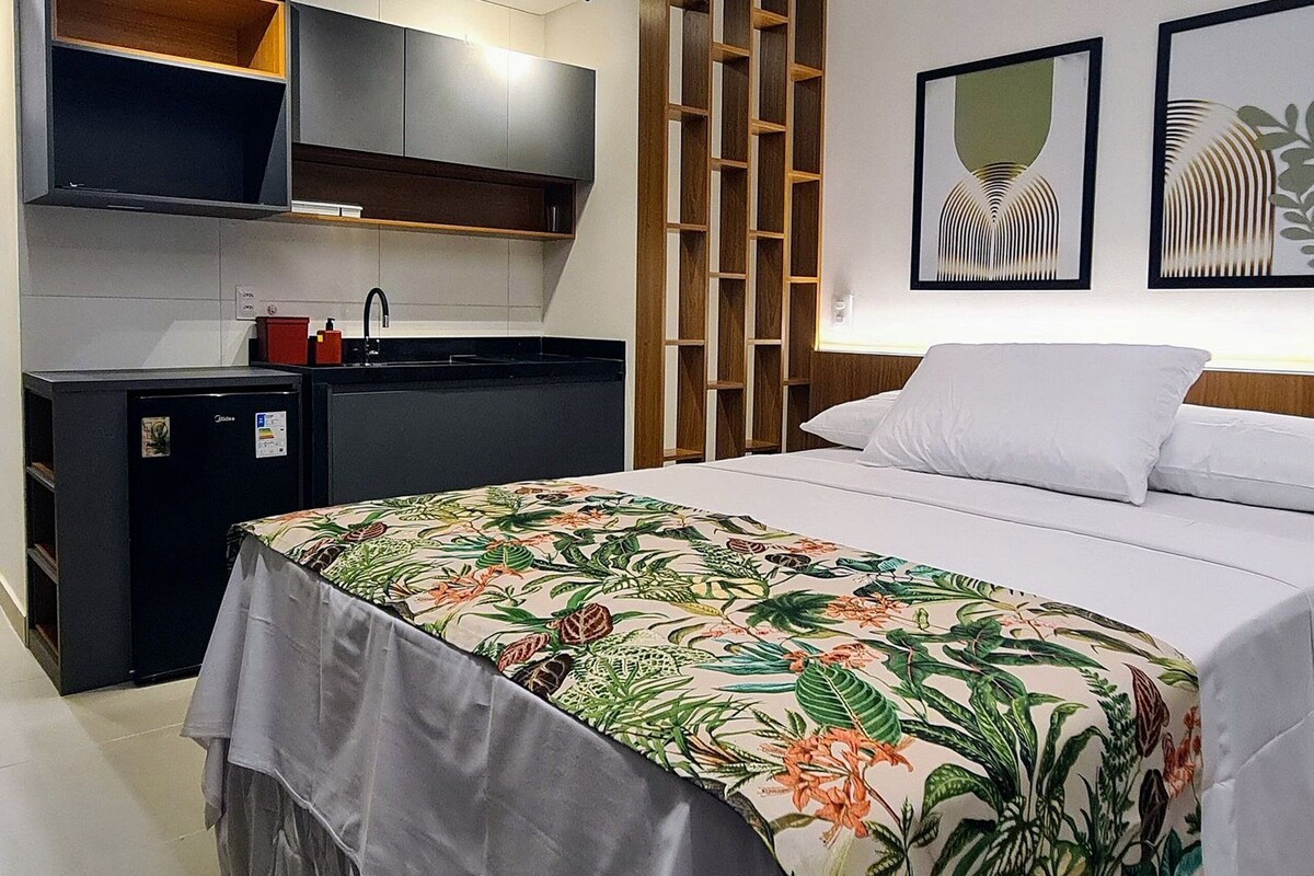 Ein modernes Hotelzimmer mit Bett, einer kleinen Küchenzeile, einer Holzauslage und zwei gerahmten Kunstwerken an der Wand.