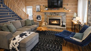 Ein Innenraum einer Blockhütte mit Wohnzimmer, Kamin, Fernseher und einer Treppe.