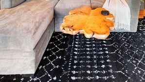 Eine gemütliche Ecke mit einem grauen Ecksofa, einem gemusterten Teppich und einer Holztreppe, die zu einem Erker führt.