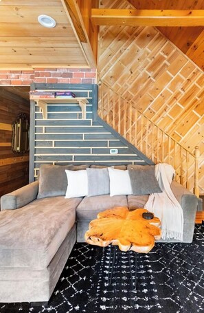 A cozy corner with a grey sectional sofa, a patterned rug, and a wooden staircase leading to a loft area. - Located in the heart of Poconos/Hottub/fireplace (Pocono Pines)