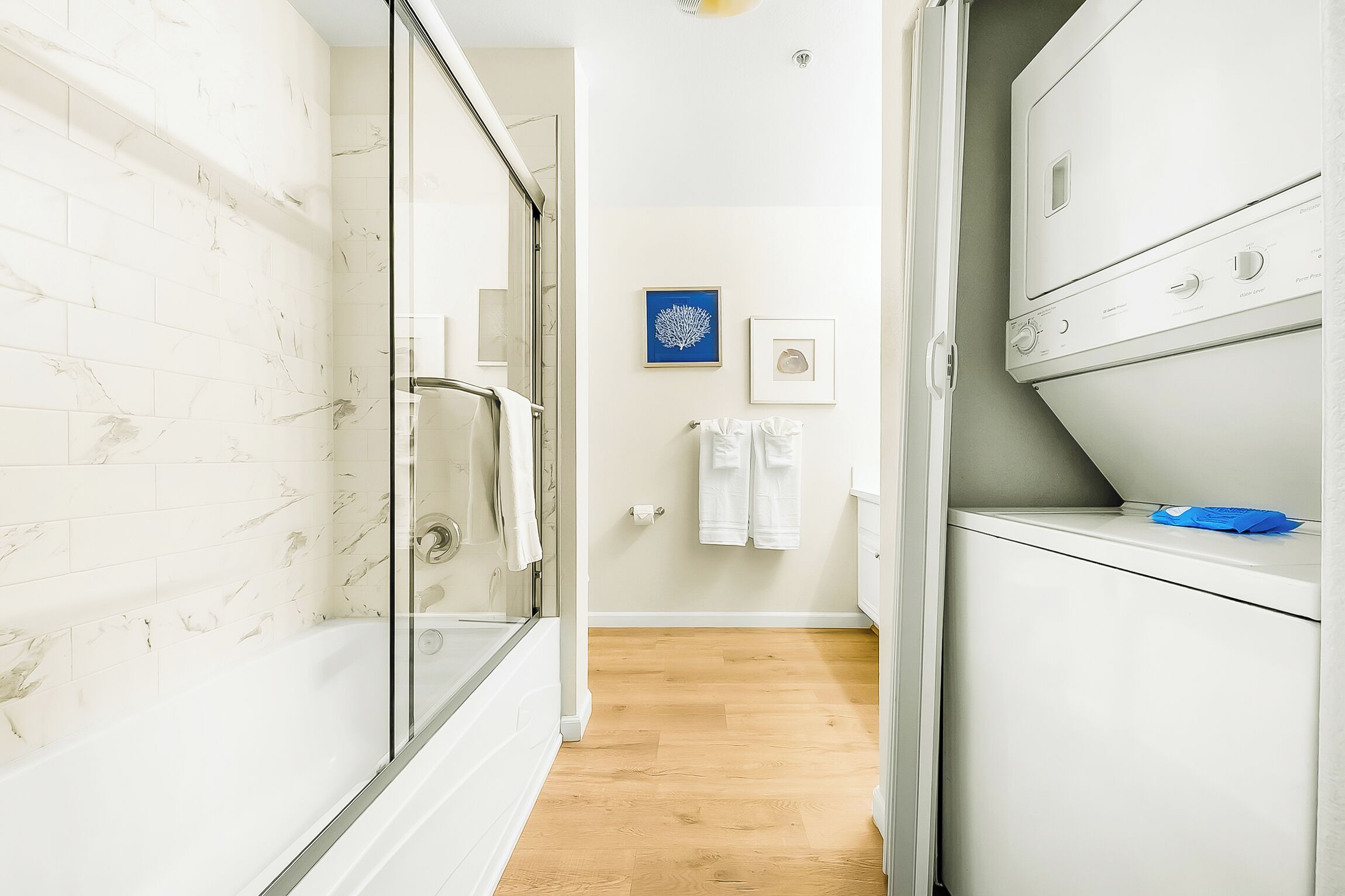 Een moderne badkamer met een douchecabine van glas, een witte badkuip en een ingebouwde wasmachine en droger.