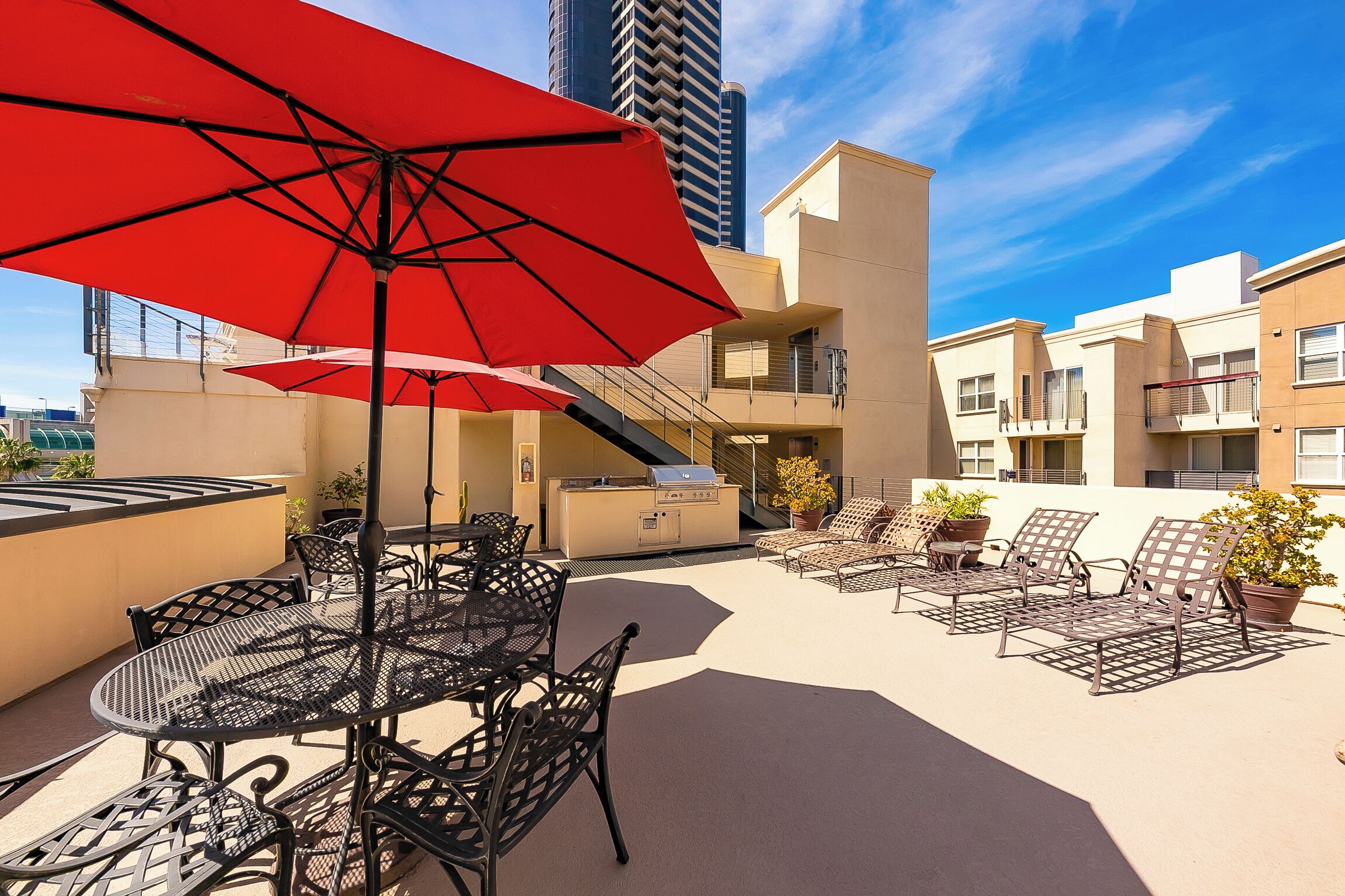 An outdoor patio with a grill, lounge chairs, and a red umbrella.
