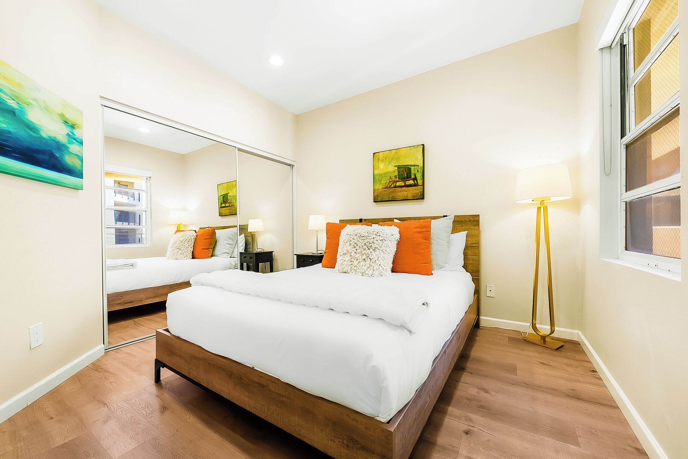 Un dormitorio bien iluminado con una cama grande, mesitas de noche, un espejo y una lámpara de pie.
